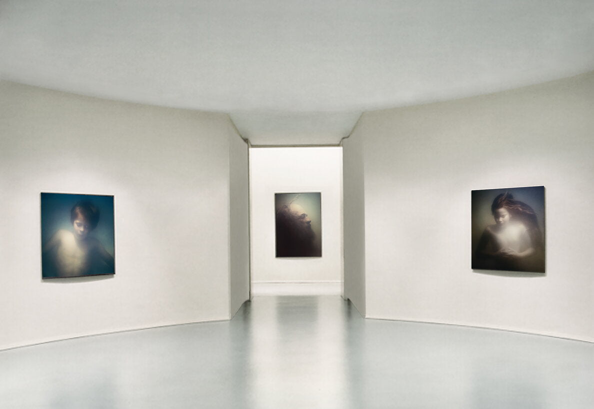An art gallery interior with three framed portrait paintings displayed on curved white walls in a softly lit gallery space.