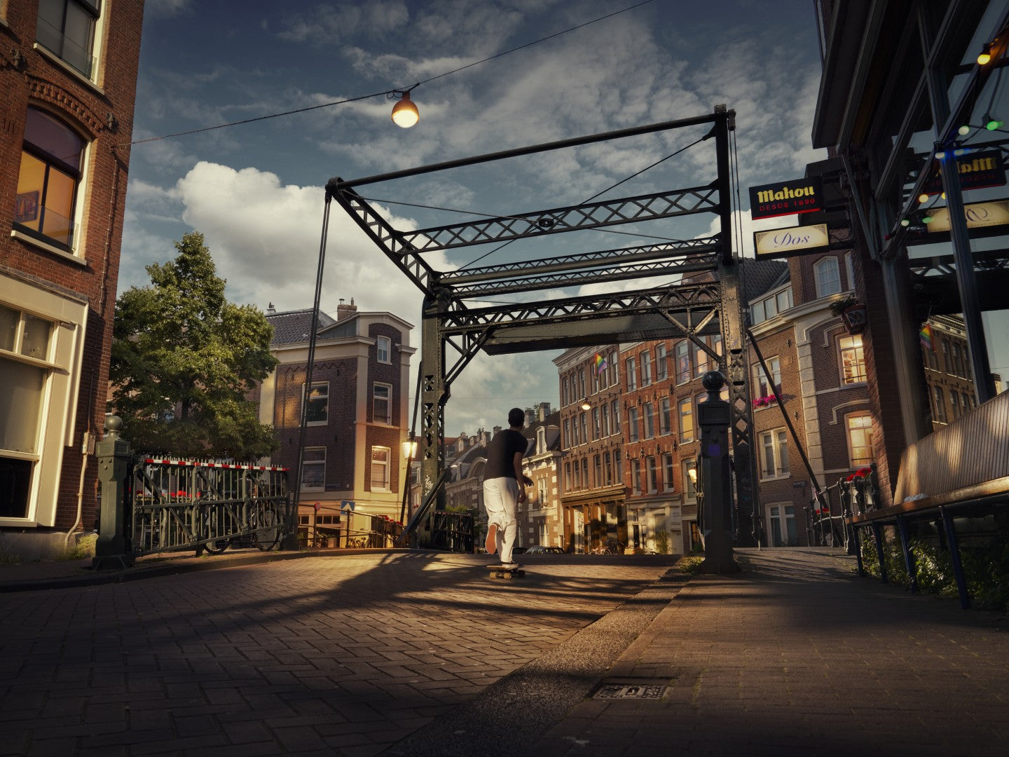 Two people standing on a street with a metal bridge and buildings in the background