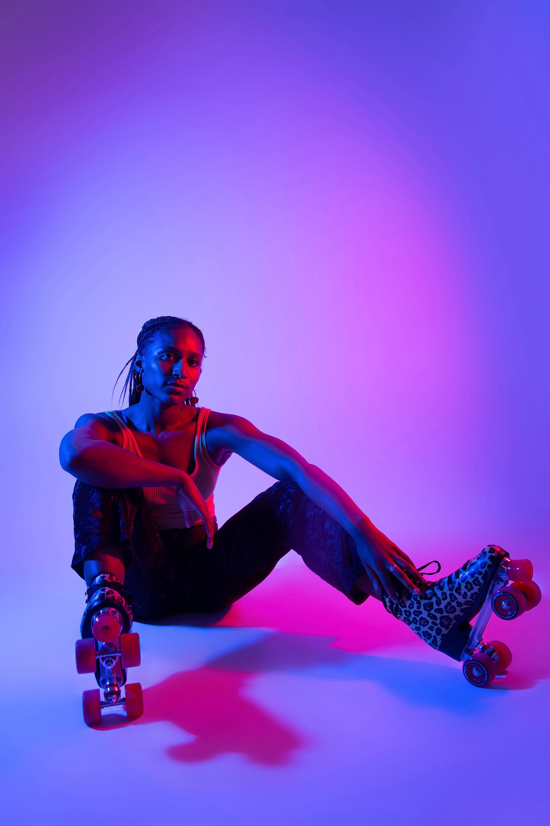 Person seated on the floor wearing leopard-print roller skates, lit by vibrant blue and pink lighting against a gradient backdrop.