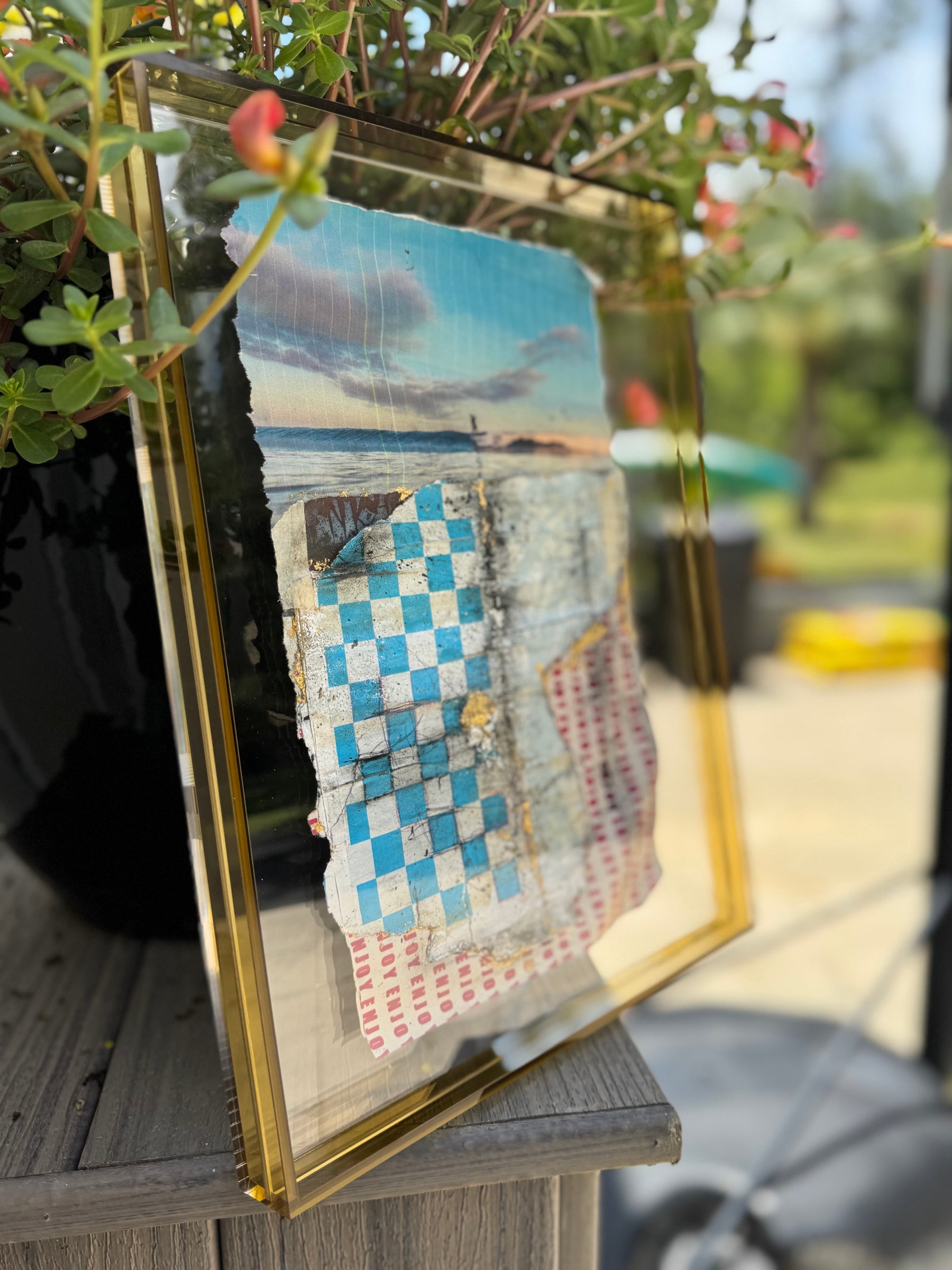 Decorative frame with a scenic beach print and checkered pattern on a blurred outdoor background