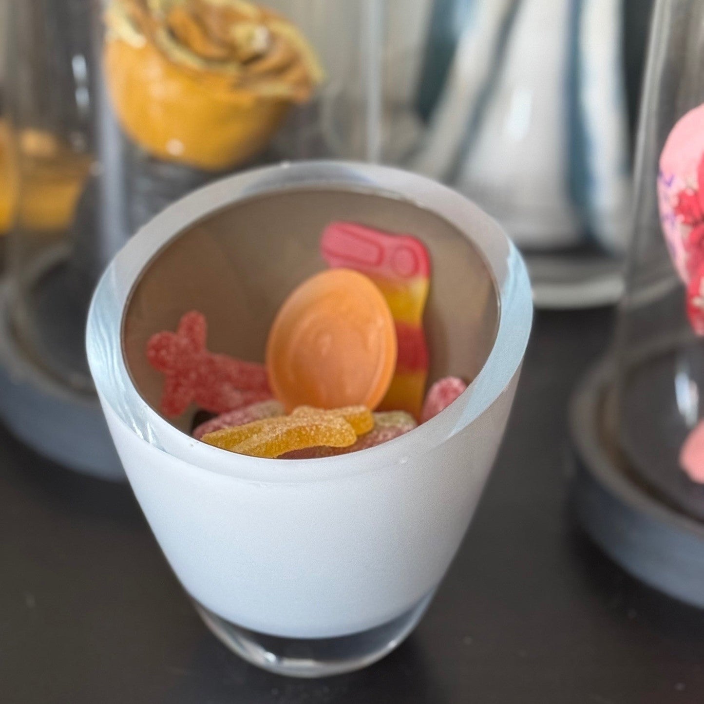 Small glass container with colorful gummy bears on a dark surface