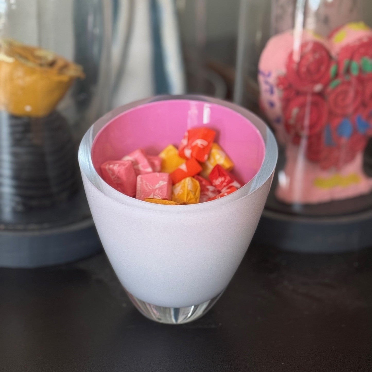 Small glass bowl with pink interior filled with colorful candy pieces on a dark surface.
