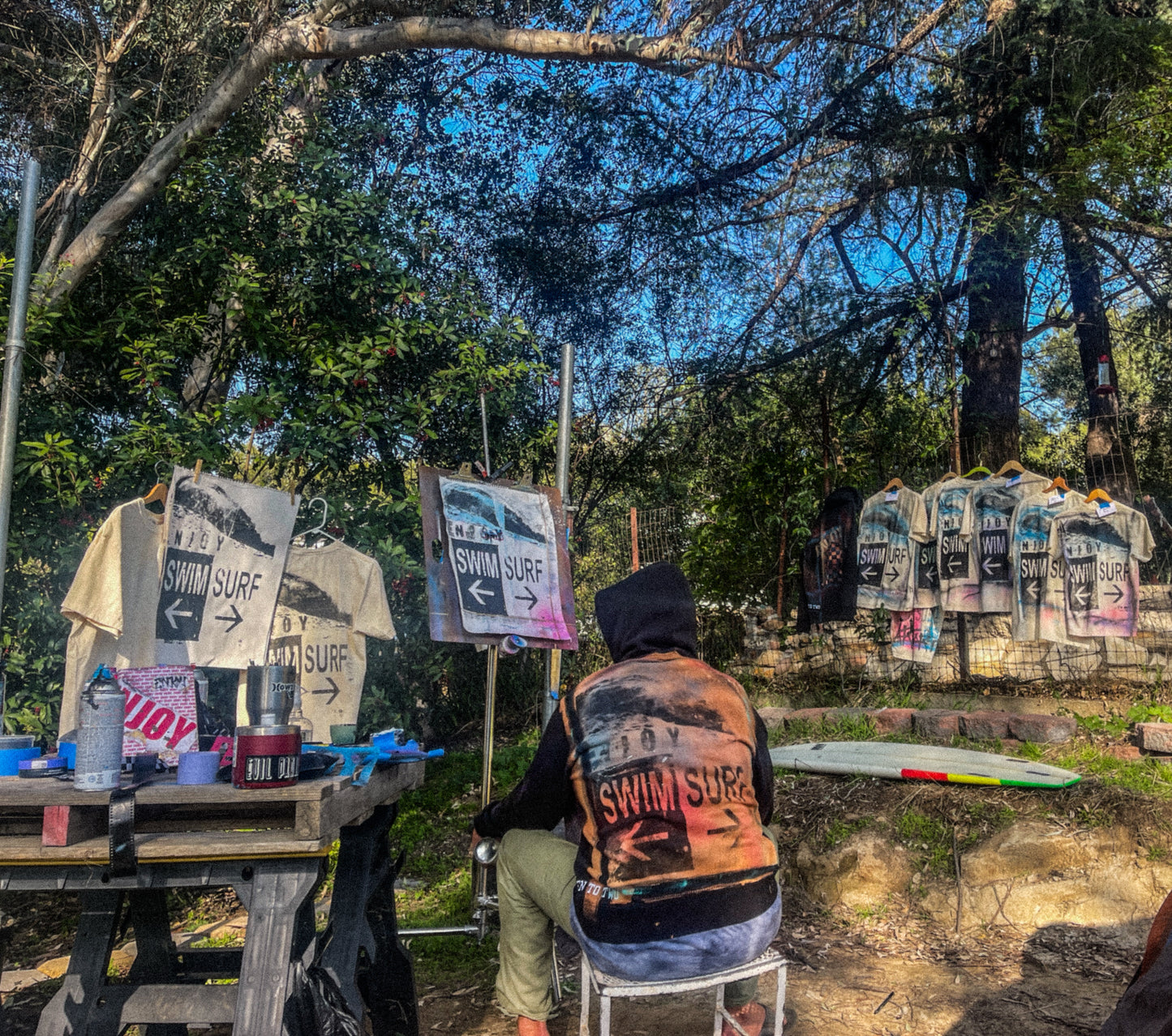 artist with hoodie with art work shirts hanging on trees
