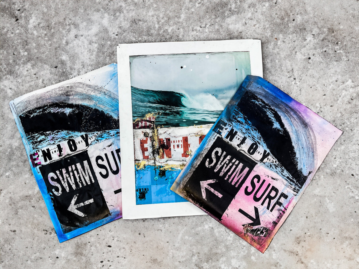 Three colorful prints with 'ENJOY SWIM SURF' text on a concrete surface