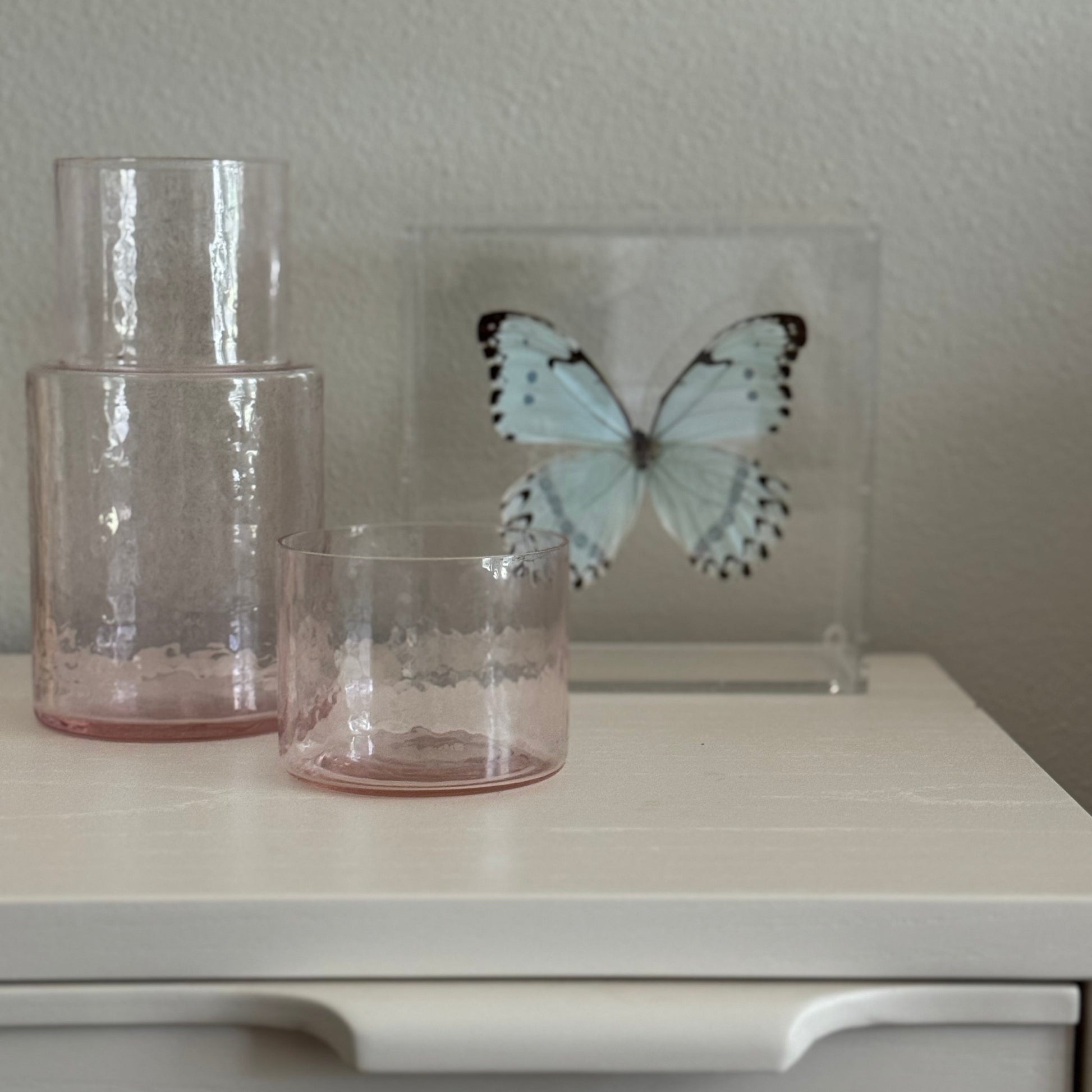 light blue and black butterfly mounted in an acrylic shadowbox sitting beside two vases.