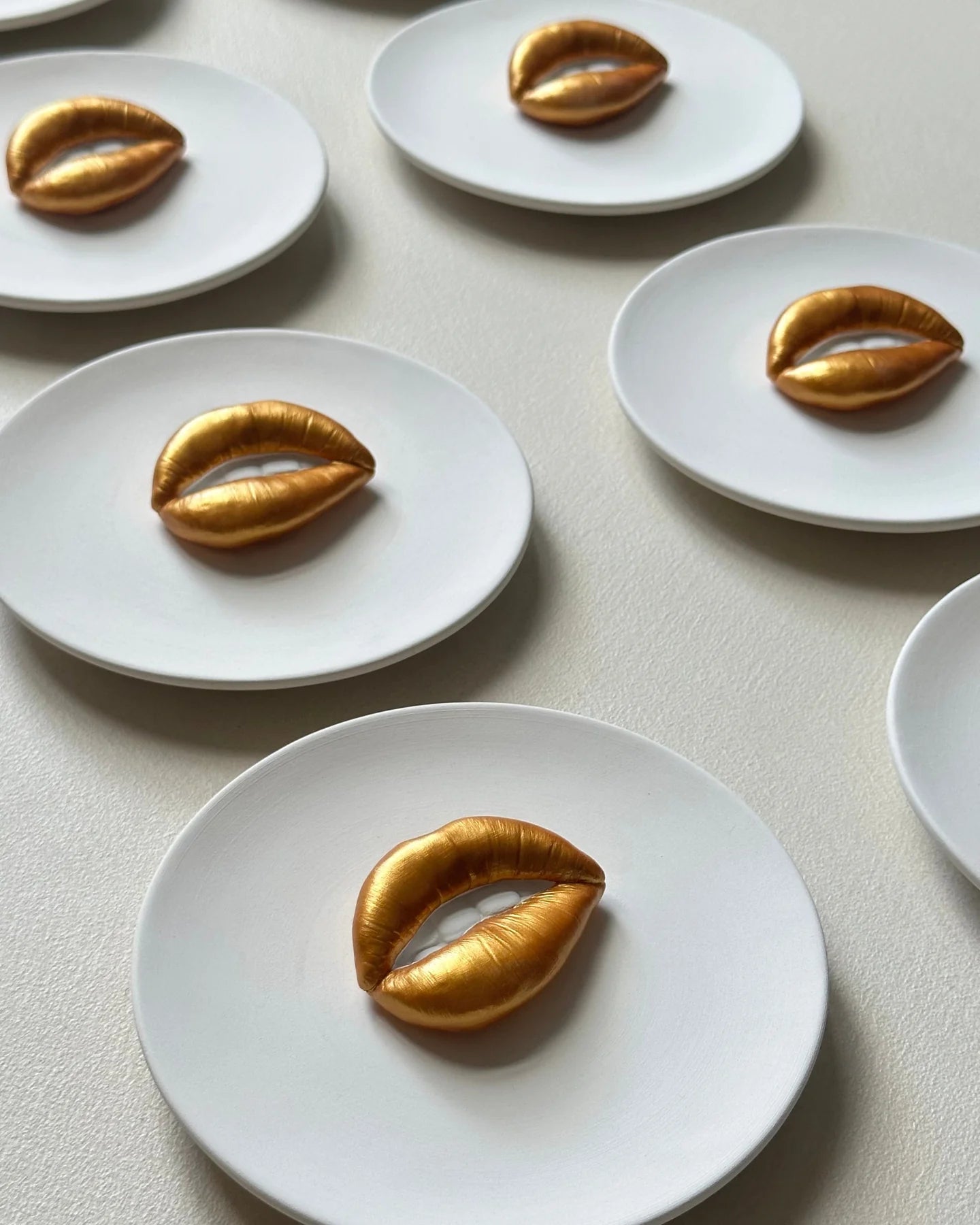Gold leaf shaped like lips on white plates arranged on a light surface