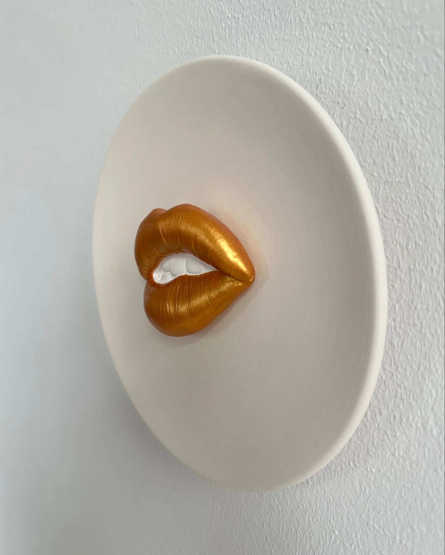 Gold lip-shaped object on a white plate against a light gray background