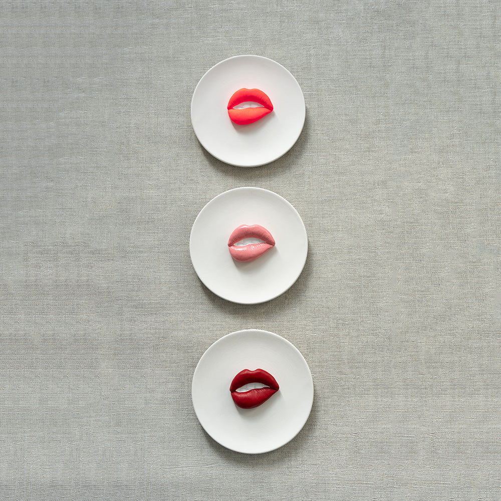 Three white plates with red, pink, and red lip-shaped objects on a gray textured background