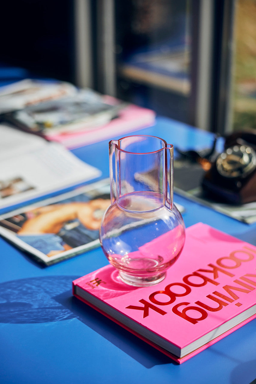 small pink glass vase on a pink look book at a blue table