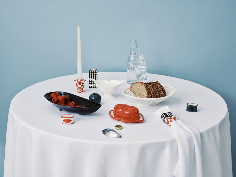 Table setting with bread, fruit, and other items on a white tablecloth against a light blue wall.