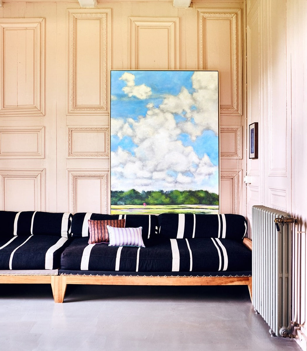 striped sofa with two striped pillows and a large painting of a sky with clouds in an ash wooden frame