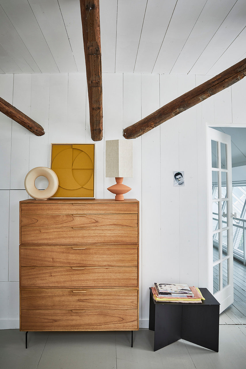 wooden dresser with terracotta table lamp and black metal side table with magazines