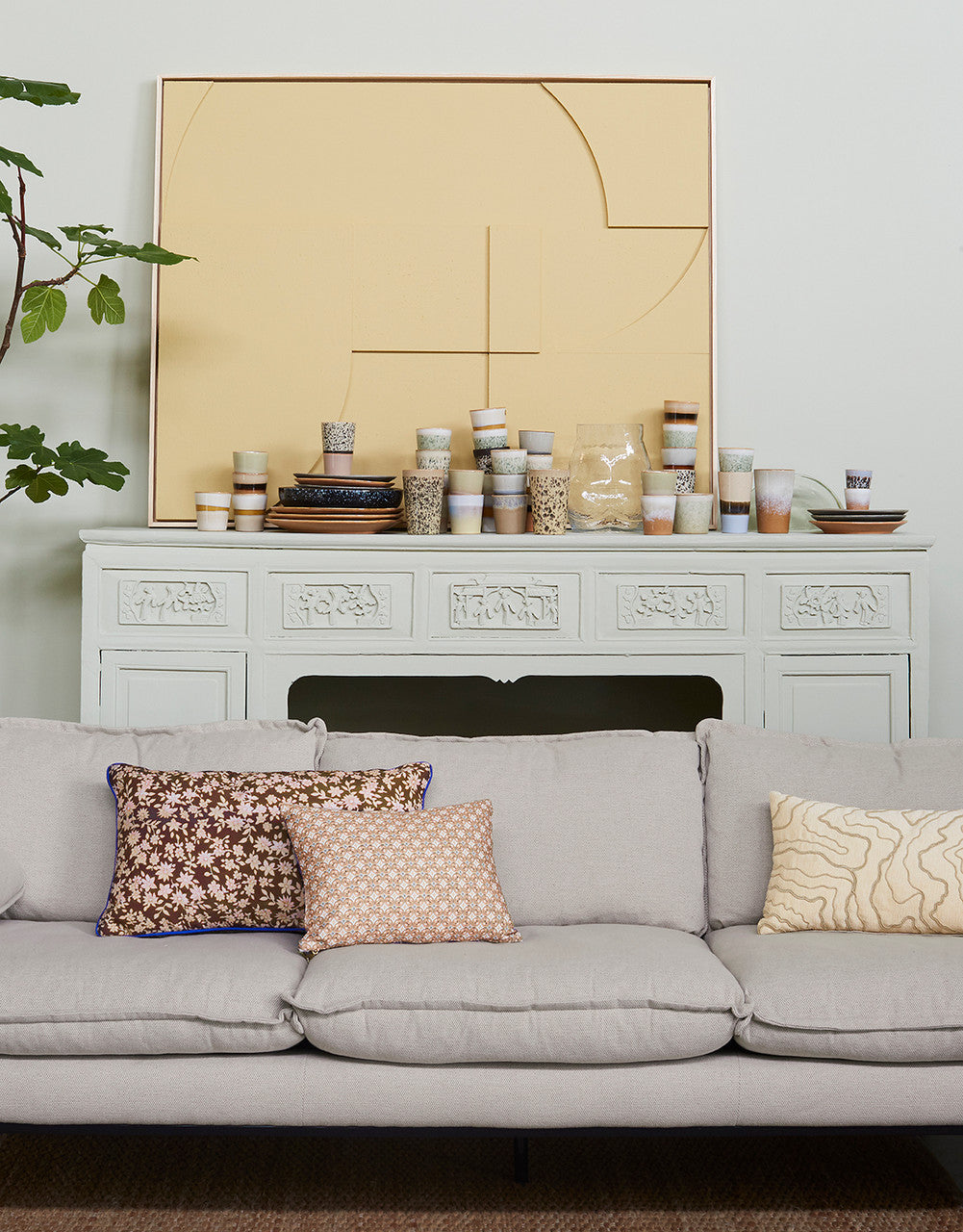 double sided lumbar pillow brown and green on a beiige sofa in front of a fire place with a large abstract art work in a wooden frame