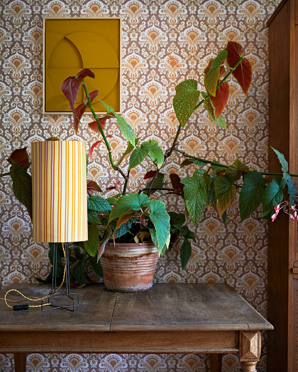striped table lamp on a black metal open base with golden cord on an antique table with a plant