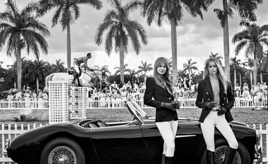 two woman in polo gear in front of Austin Martin with horses on polo field and palm trees in back ground 