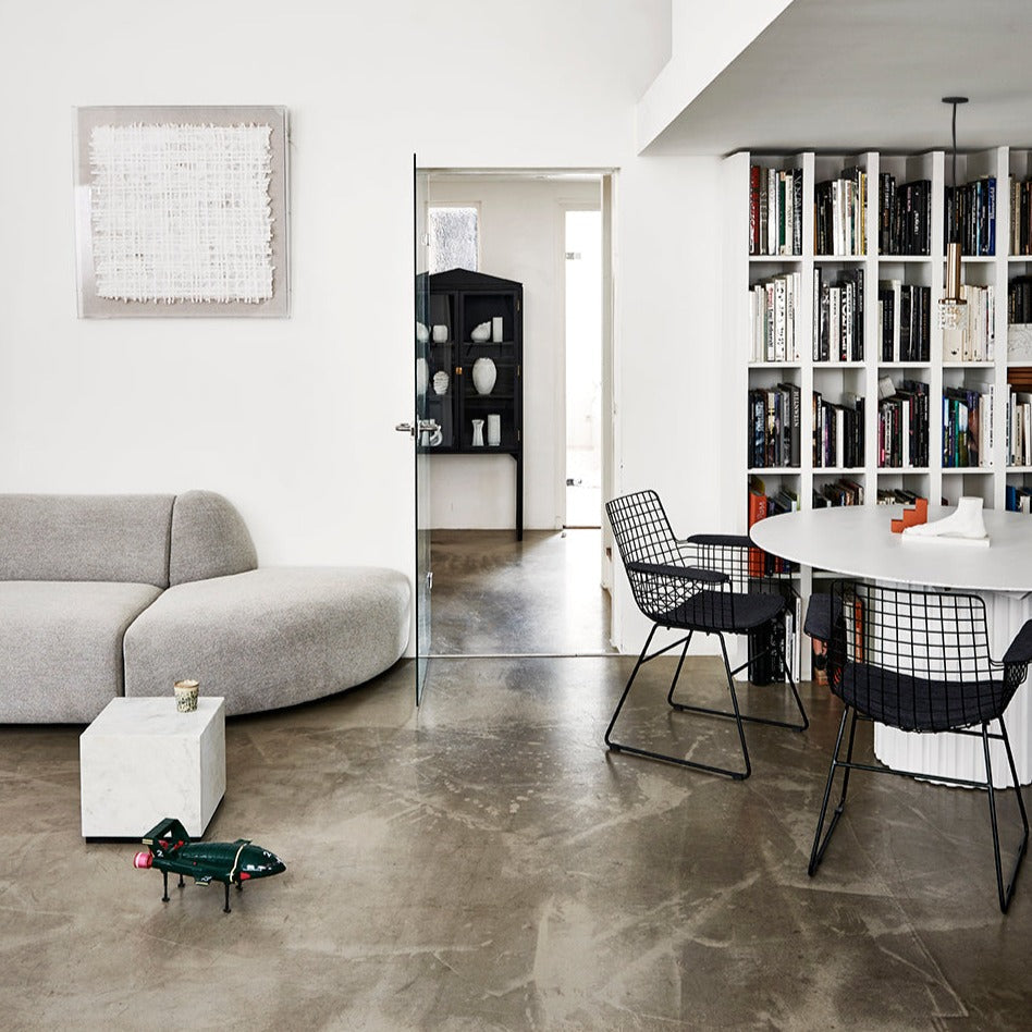 Modern black and white minimalist living room with sculptural gray sofa, marble side table, wire dining chairs, round white table, and built-in bookshelf in contemporary interior design.