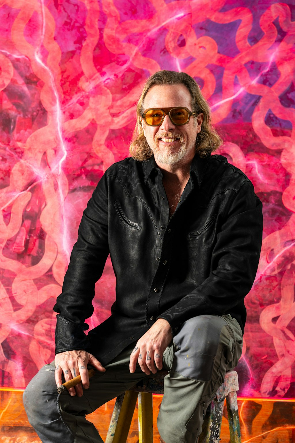 man with glasses sitting in front of bright color painting
