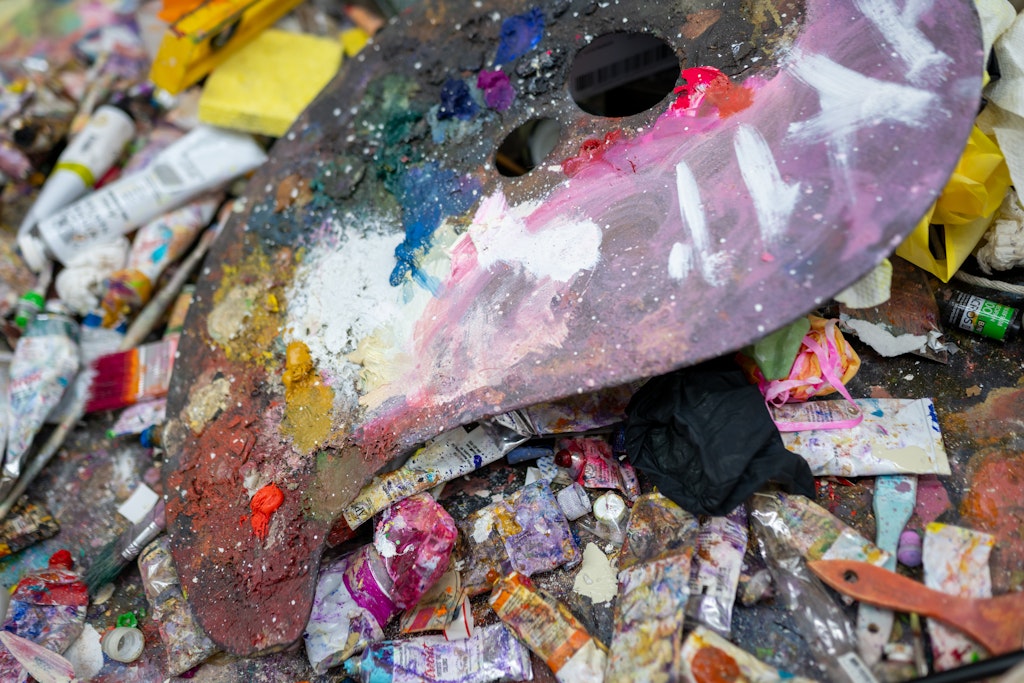 Artistic paint palette with colorful paint splashes surrounded by paint tubes and containers.