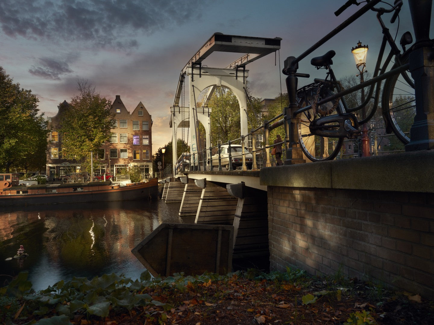 Bicycle leaning against a bridge over a canal with buildings and streetlights in the background.