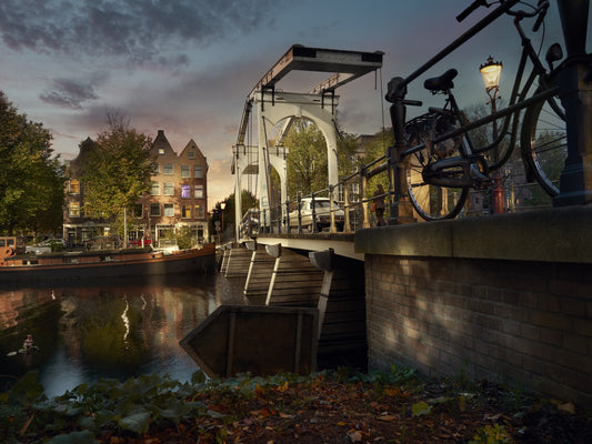 Bicycle leaning against a bridge over a canal with buildings and streetlights in the background.