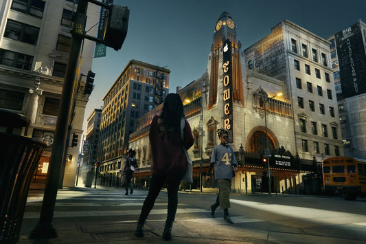 Two people walking on a city street with a prominent building labeled 'Tower' in the background.