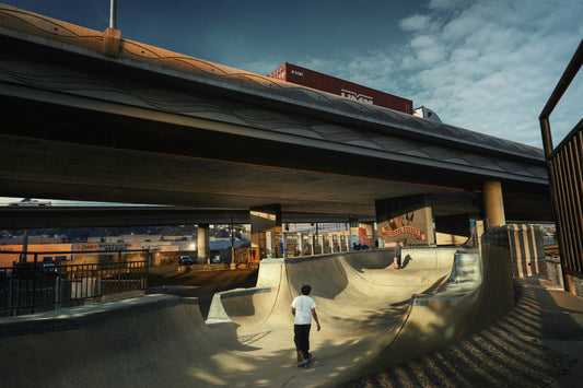 Skateboarder at a skate park under an overpass with a train in the background
