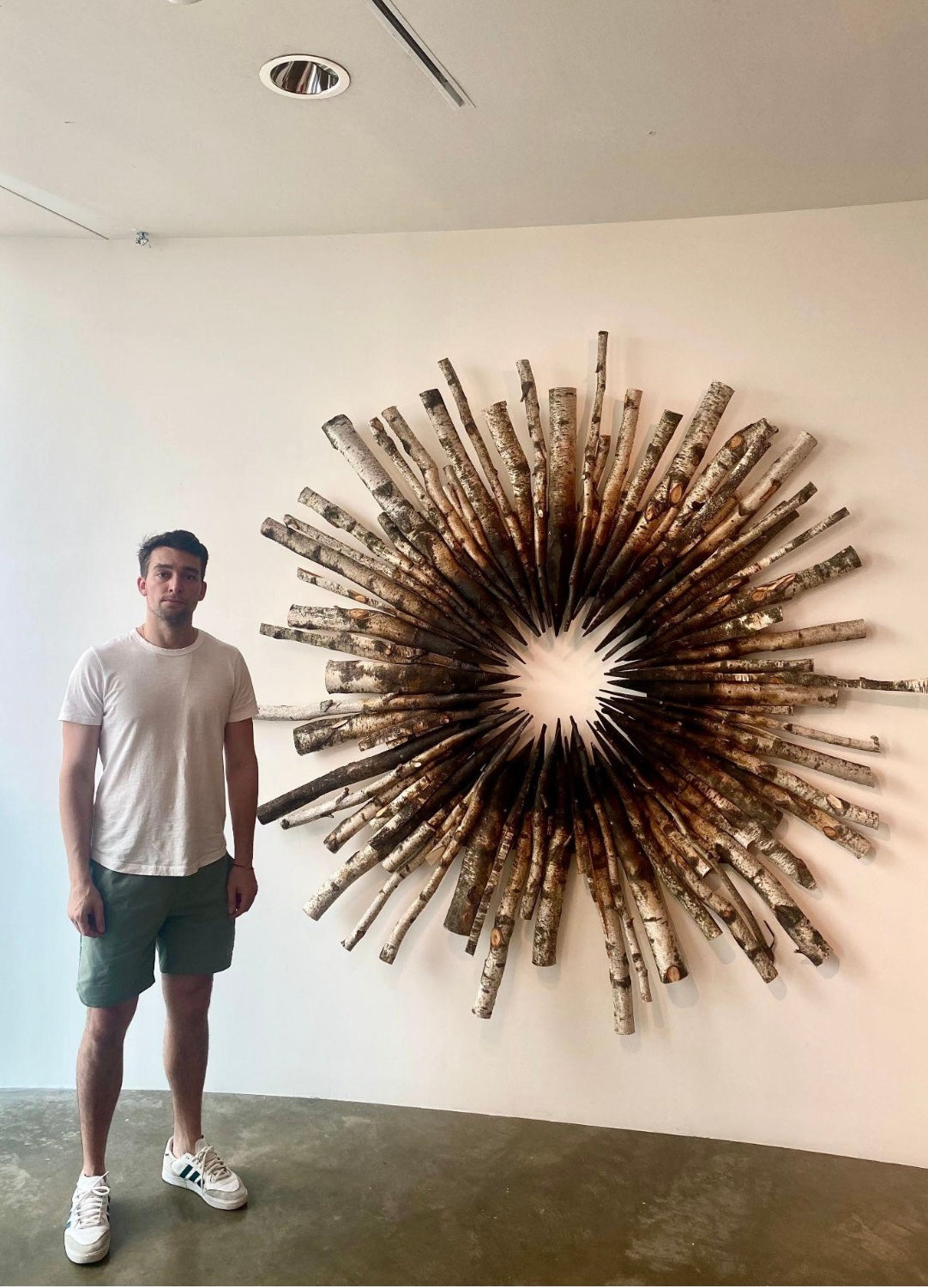Man standing next to a large wall art piece resembling a sunburst design.
