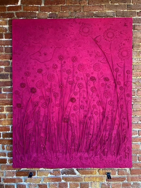 Pink mixed media art work with a floral pattern hanging on a brick wall.