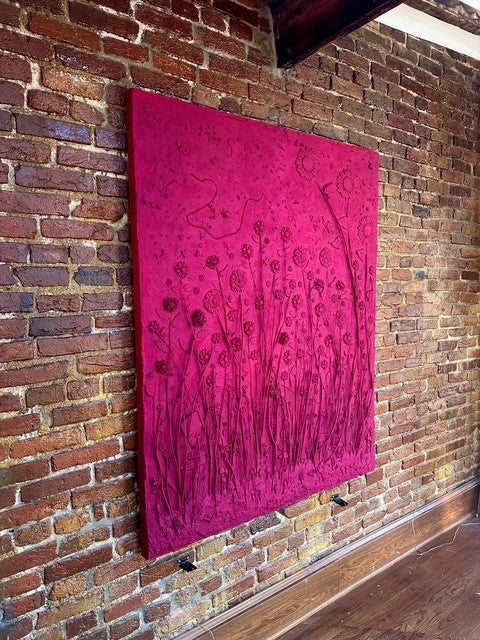 Pink mixed media art work with a floral pattern hanging on a brick wall.