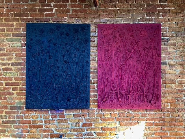 Two textured rugs, one blue and one pink, against a brick wall.