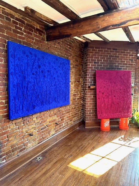 Two abstract paintings, one blue and one pink, on a brick wall with wooden beams.