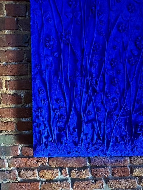 Blue textured artwork leaning against a brick wall