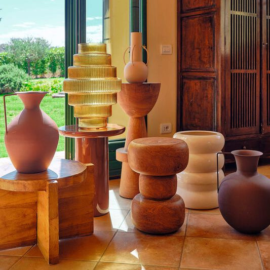 Decorative vases and wooden stools on a tiled floor with a large window in the background.