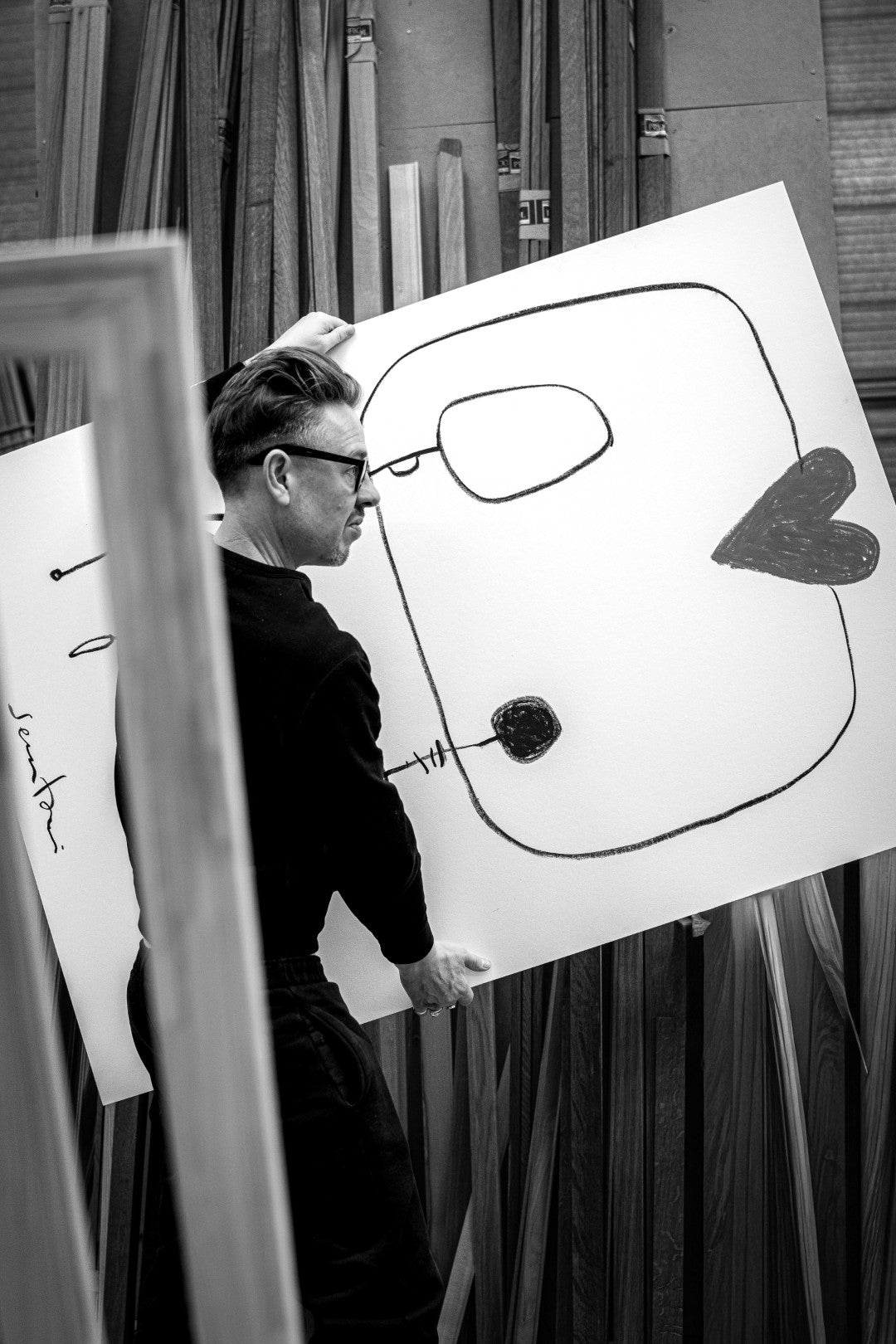 Person holding a large drawing of a face with minimalistic design in an indoor setting.