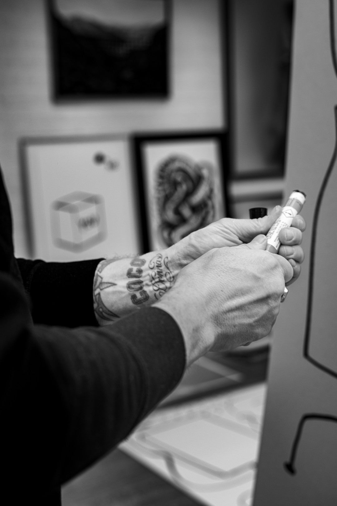 Person with tattooed hands holding a marker, with tattoo designs in the background