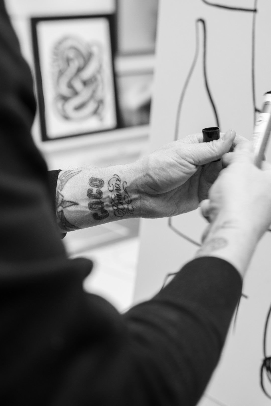 Person with tattooed arm holding a tattoo machine, working on a design.