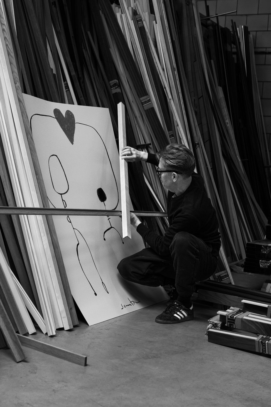 Person working on a large art piece with a heart symbol in a workshop setting.