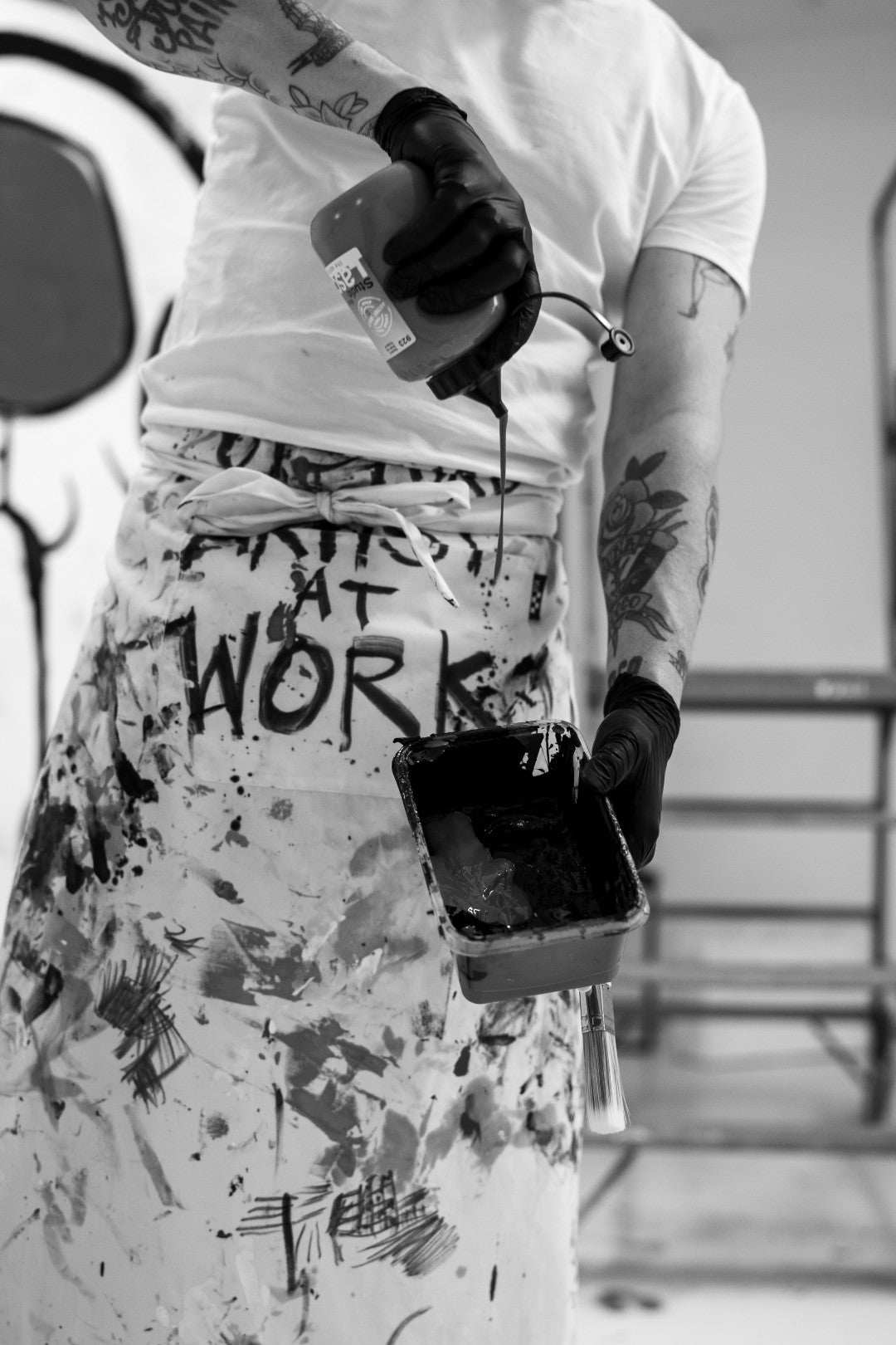 Person wearing a white t-shirt and patterned pants with text, holding a phone and a bottle.