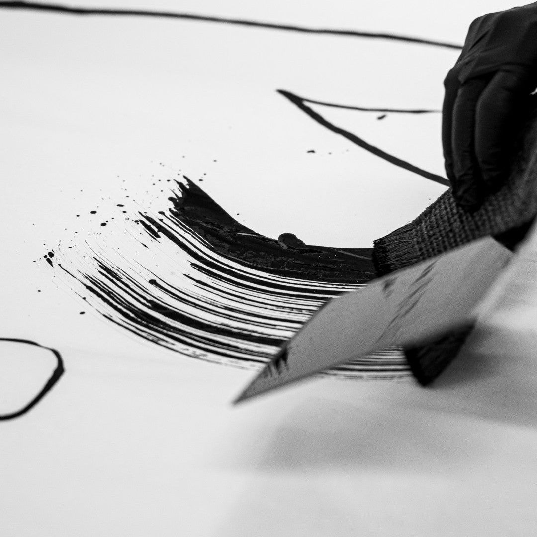 Person using a brush to draw on a large sheet of paper with black ink.