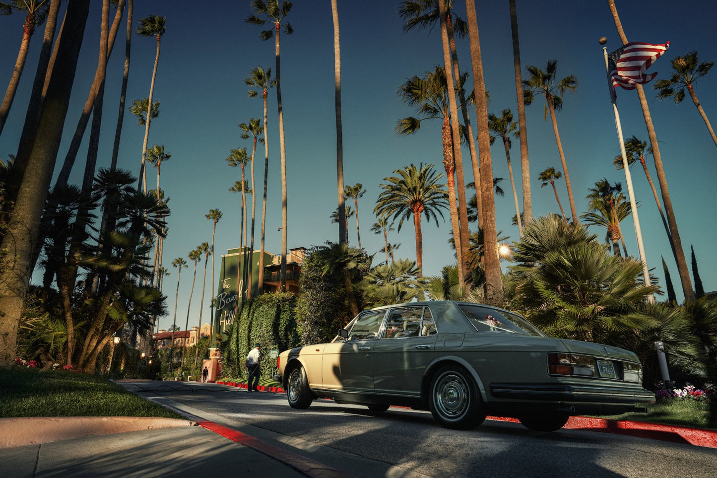 Vintage car parked on a street lined with palm trees and American flags.
