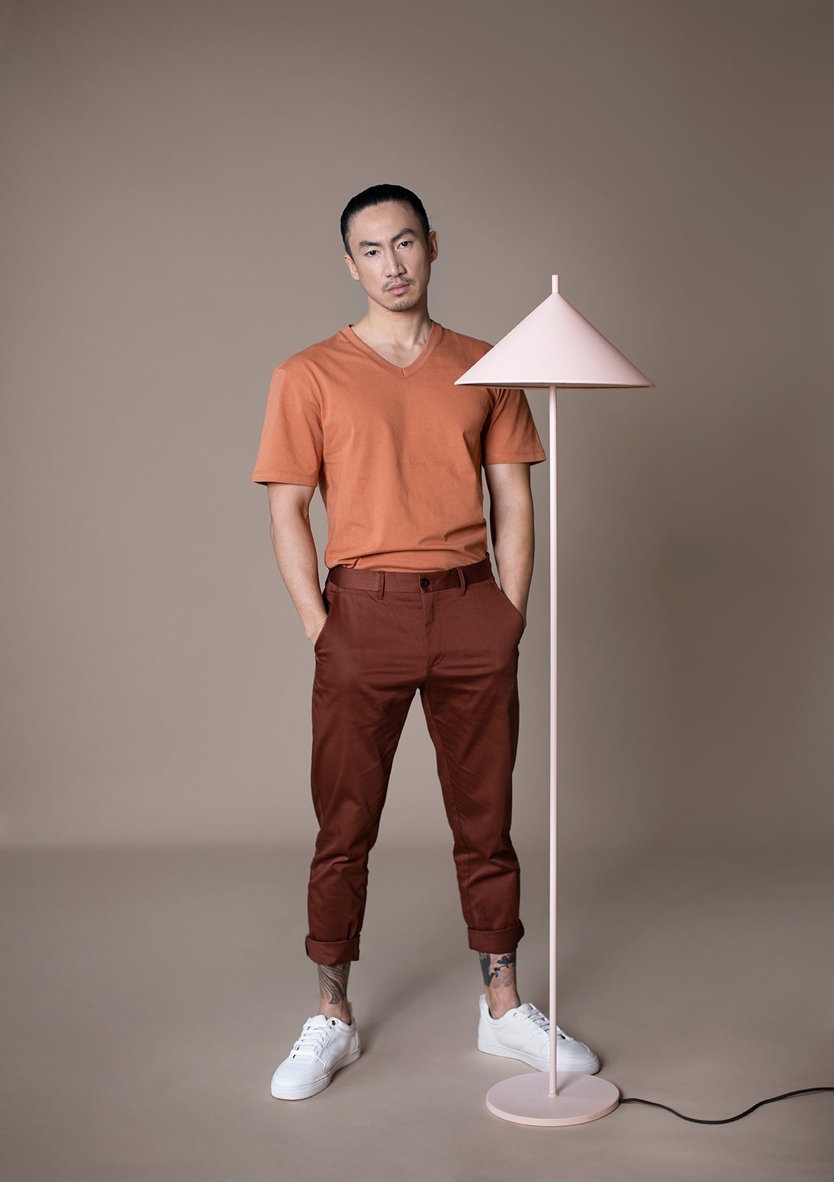 man with orange shirt, maroon pants next to a blush colored metal triangle floor lamp