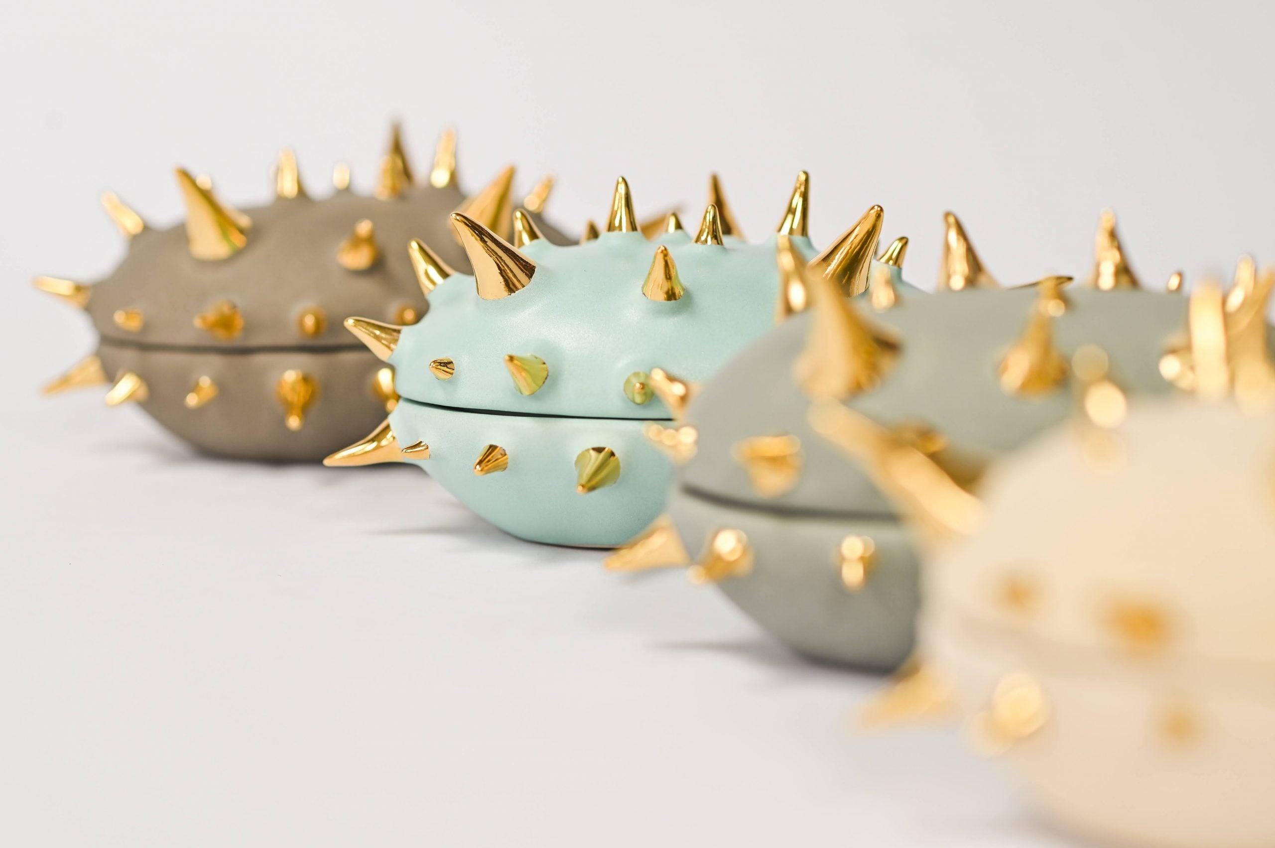 Close-up of Waylande Gregory spiked capsule boxes in muted pastel tones with glossy 22k gold spikes; modern handmade ceramic decor.