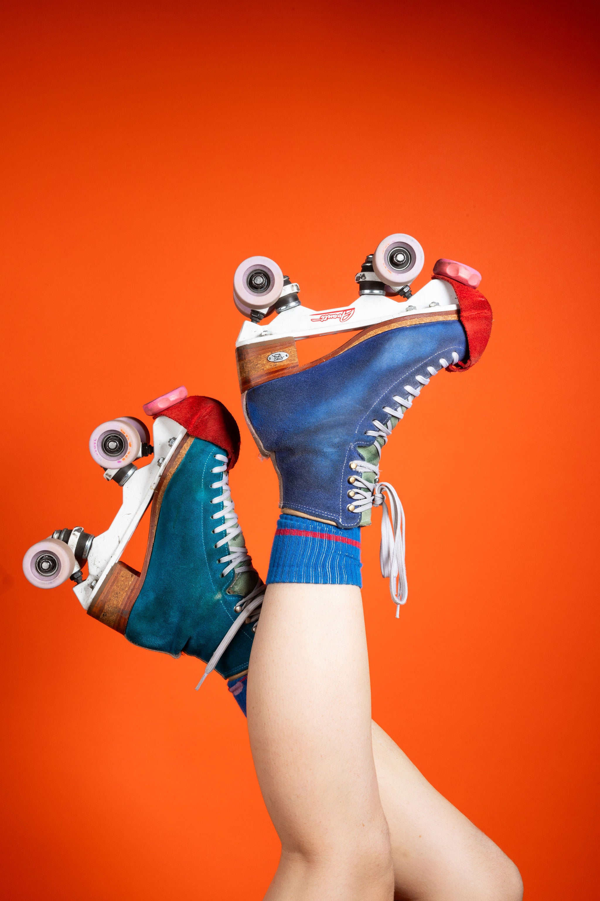 Person with crossed legs raised, wearing vintage-style roller skates in blue against an orange background.