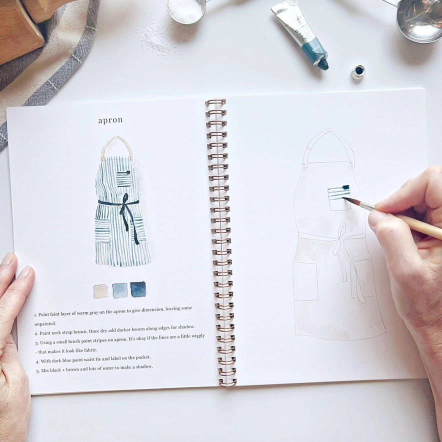 open work book with illustration and a hand holding a small brush