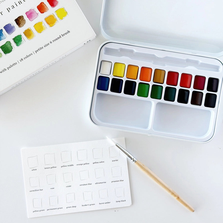 water color blocks and a brush in a white tin with a  coloring card