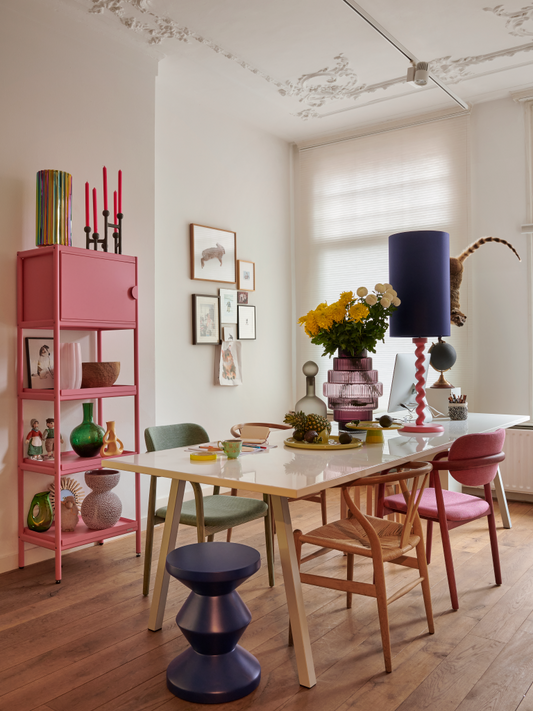 large purple glass vase with flowers on a table with colorful chairs