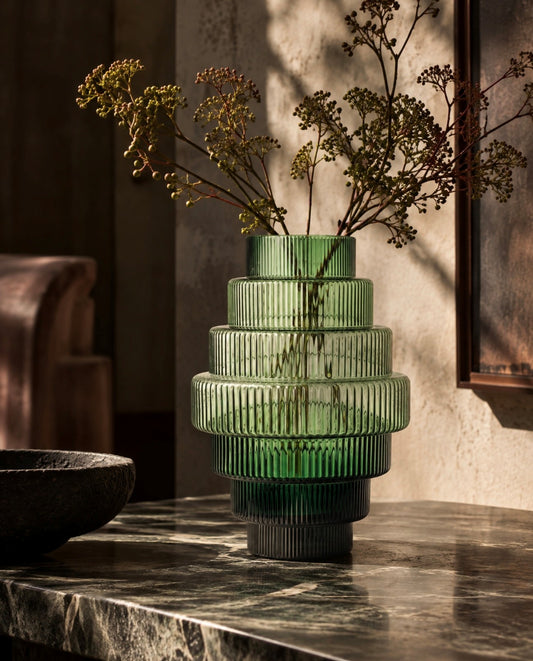 olive green glass vase with branches on a black marble surface