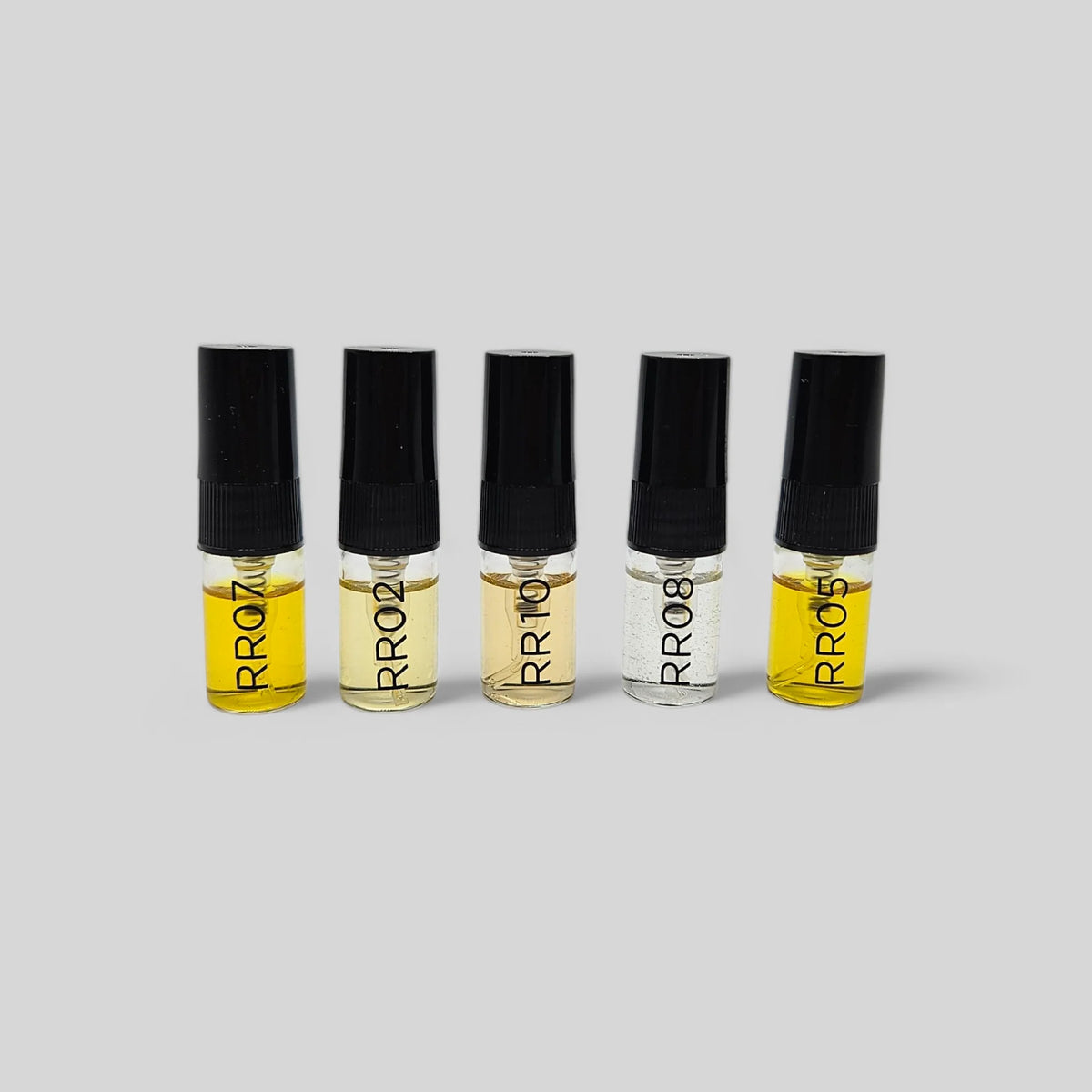 Five small glass perfume sample vials with black caps arranged in a row on a light gray background. The vials contain yellow, beige, and clear liquids, and each is labeled with the brand name 'RR08'.