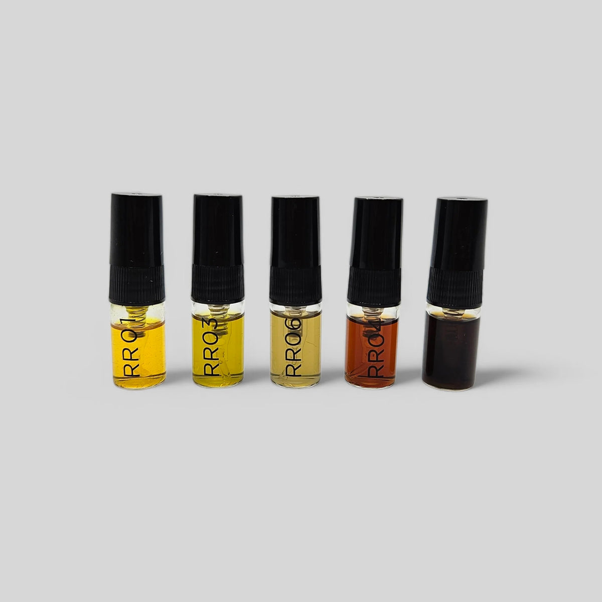 Five small glass sample vials with black caps arranged in a row on a light gray background. The vials contain liquids in amber, golden yellow, and dark brown shades, with the brand name 'RR06' printed vertically on each bottle.
