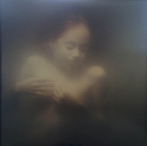 A soft-focus, painterly artwork depicting a nude female figure with a blurred face, rendered in muted dark gray and warm beige tones.